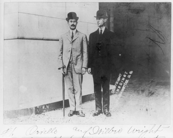 Orville and Wilbur Wright standing together in suits and derby hats.